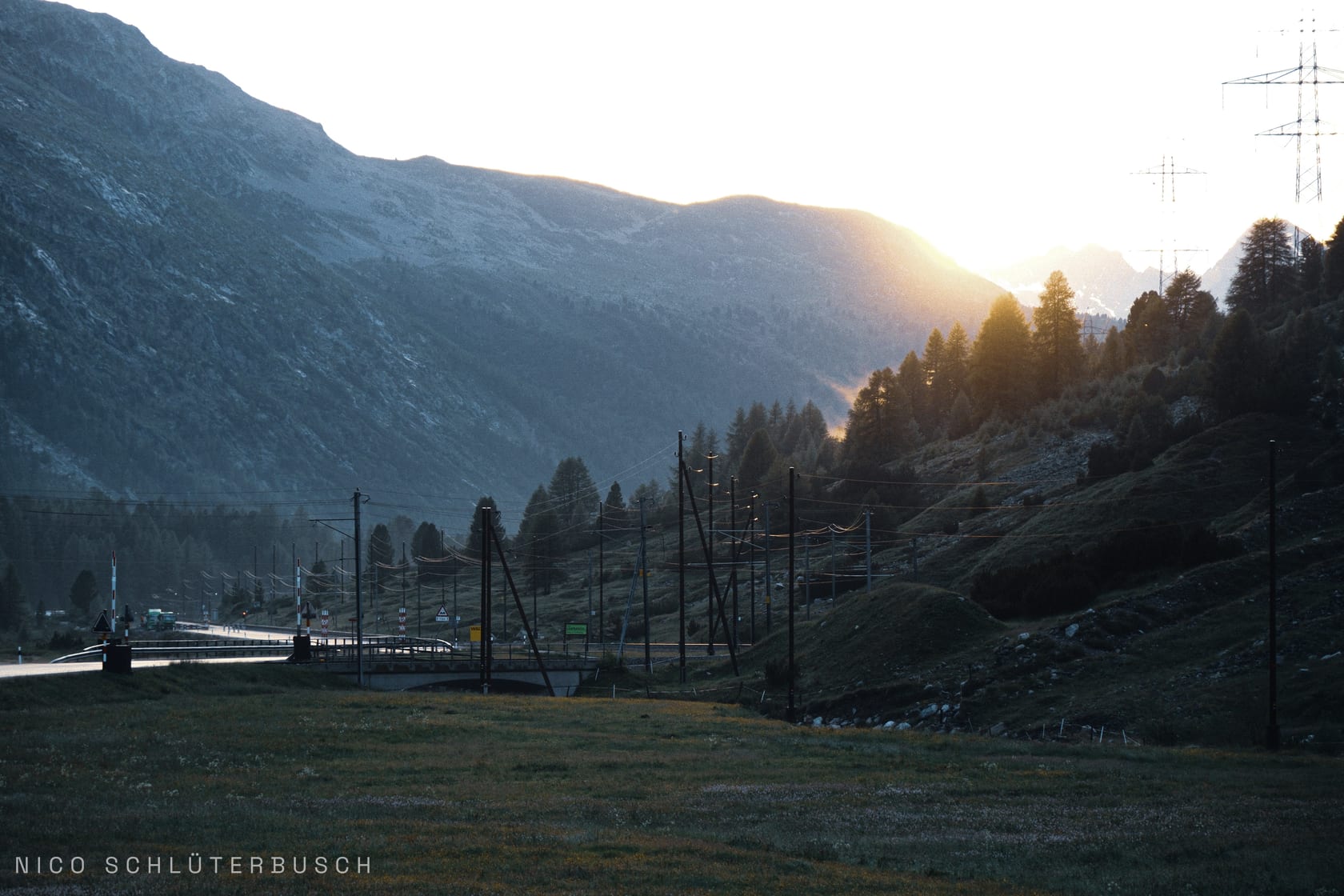 Sonnenuntergang über einem Alpental mit Passstraße und Bahntrasse