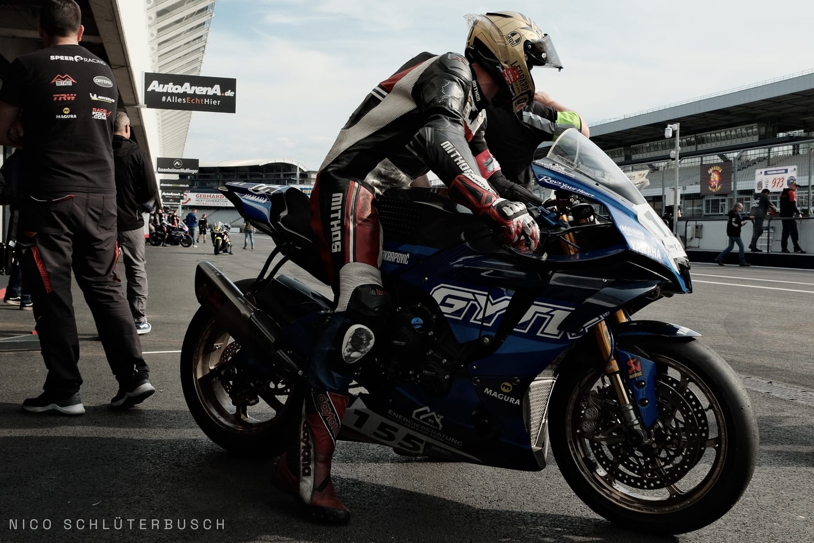 Rennfahrer in Lederkombi steigt in der Boxengasse auf eine blaue Yamaha mit Startnummer 155.