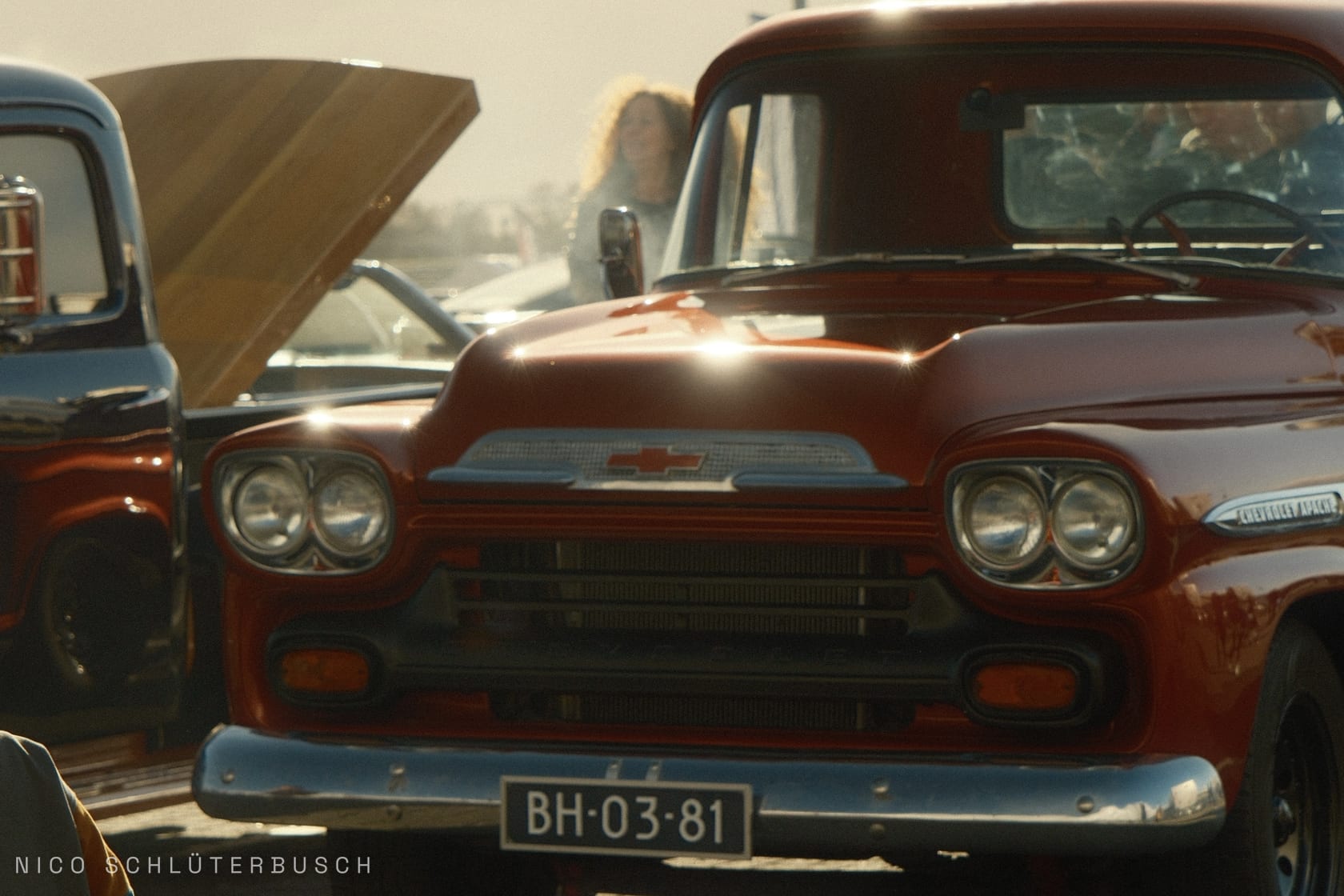 Roter Chevrolet Apache Pickup in der Frontansicht mit Chromgrill und Doppelscheinwerfern im Gegenlicht eines Oldtimertreffens