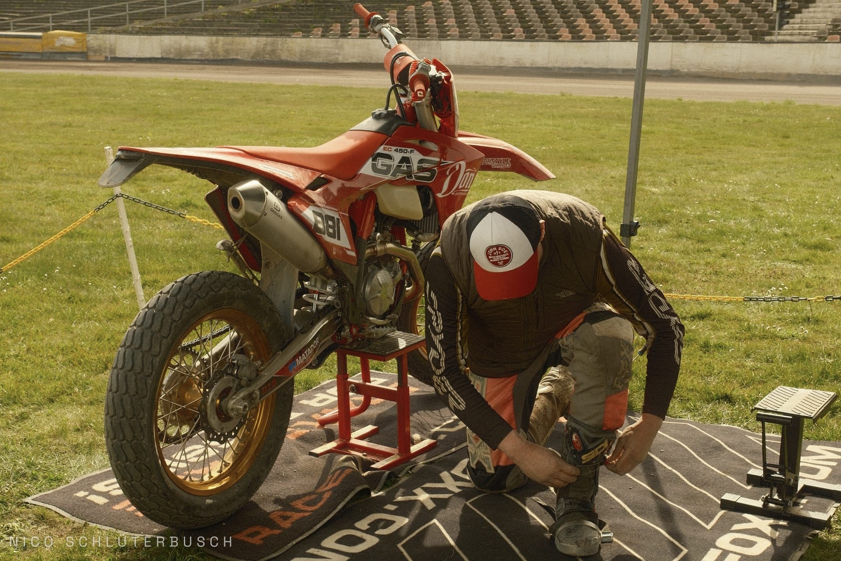 Rote GasGas EC 450-F mit Startnummer 81 auf einem Montageständer im Speedway-Stadion, daneben kniet ein Fahrer und verschließt seinen Stiefel.