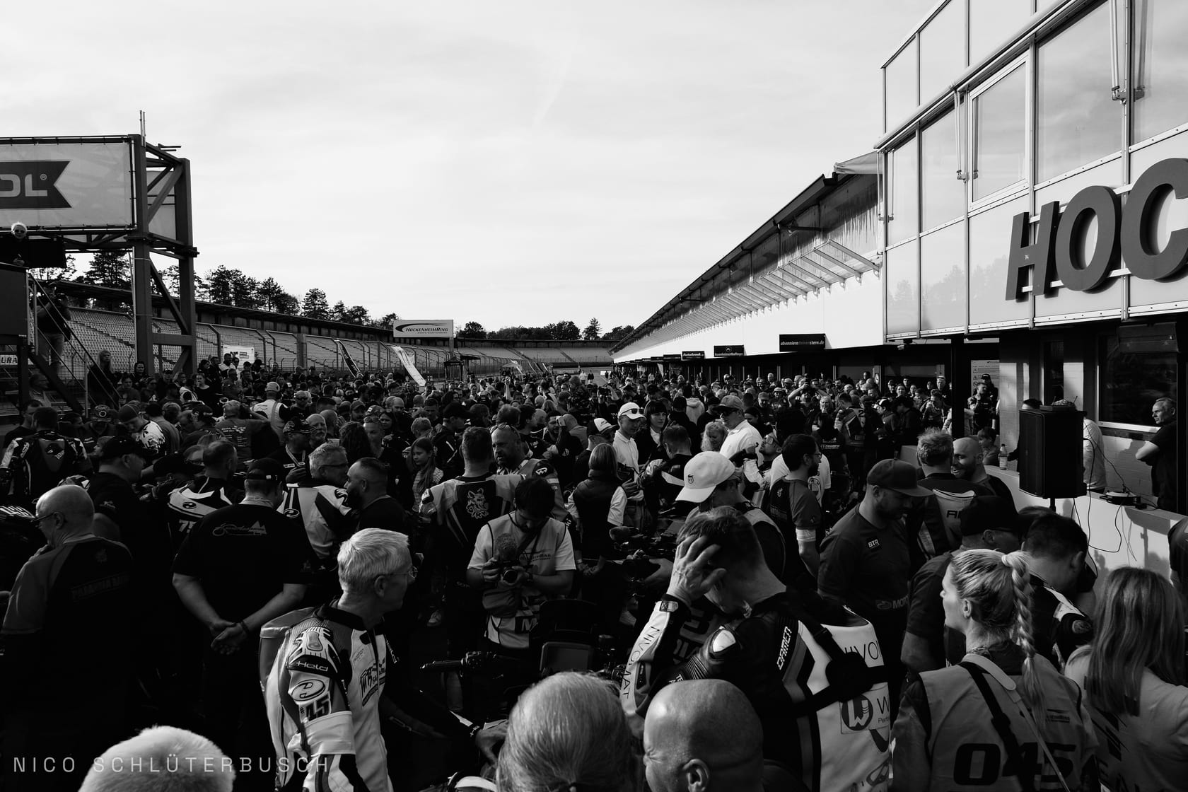 Dichte Menschenmenge aus Fahrern in Lederkombis und Besuchern in der Boxengasse des Hockenheimrings in Schwarz-Weiß