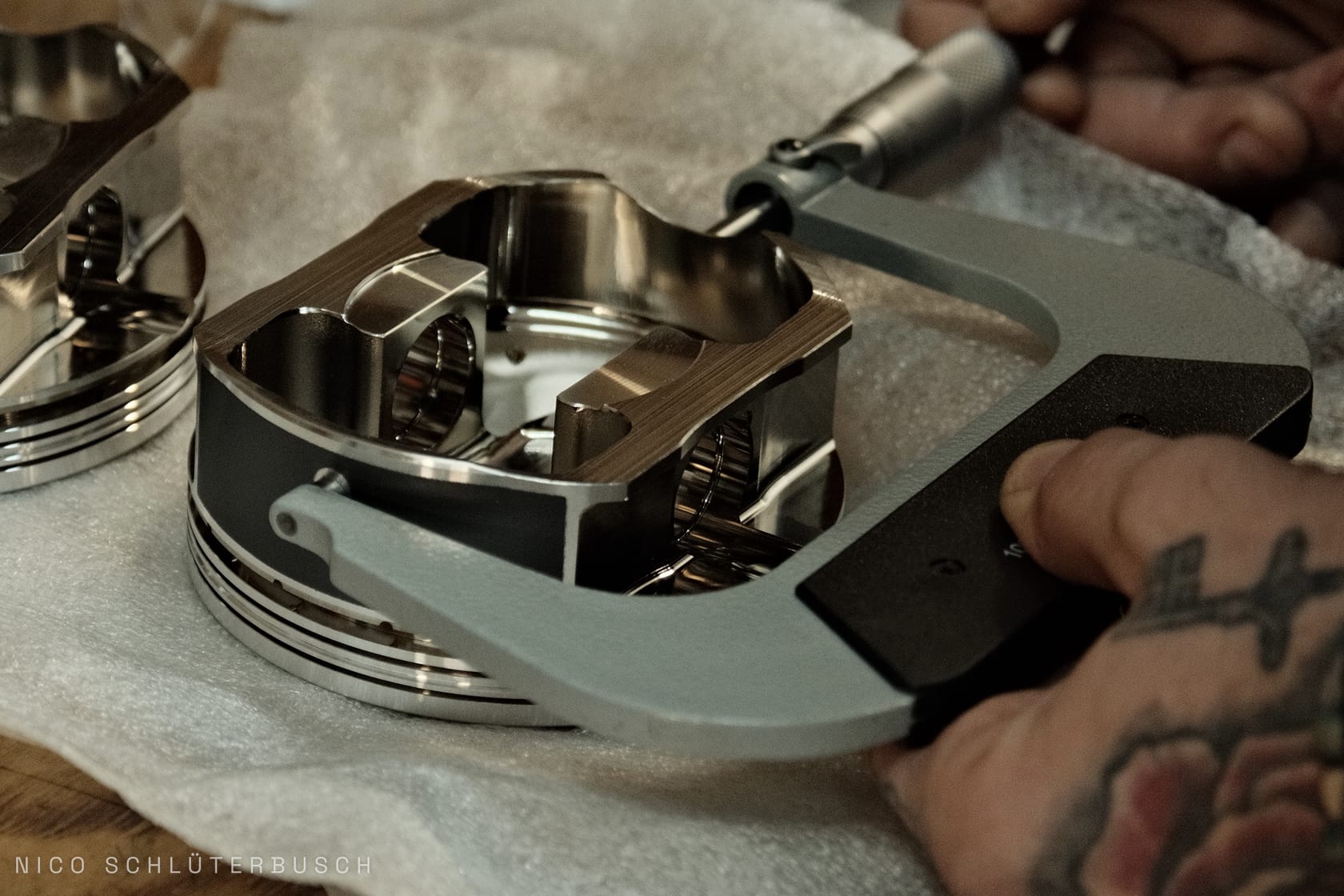 Tätowierte Hände vermessen einen polierten Schmiedekolben mit einer Bügelmessschraube auf Luftpolsterfolie
